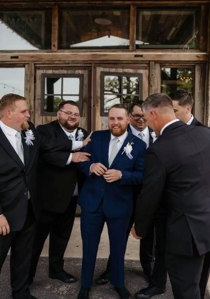 Groom laughing with groomsmen outside rustic barn wedding venue Oklahoma