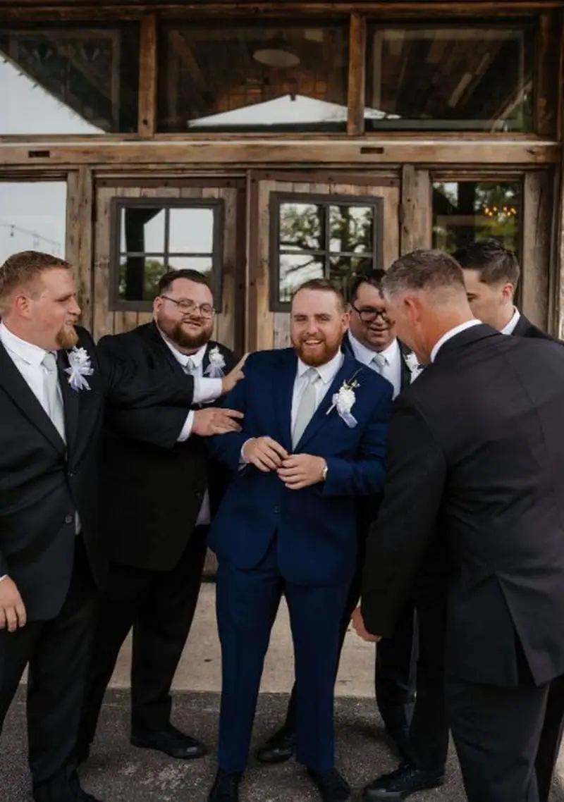 Groom laughing with groomsmen outside rustic barn wedding venue Oklahoma